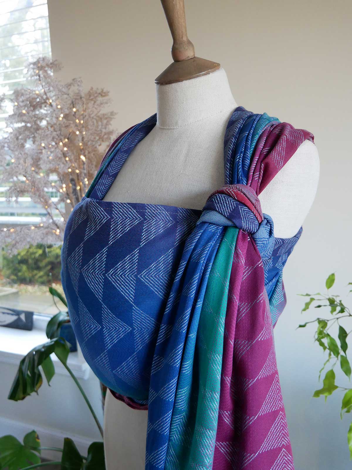 Mannequin wearing a colourful woven wrap with geometric patterns in a home setting.