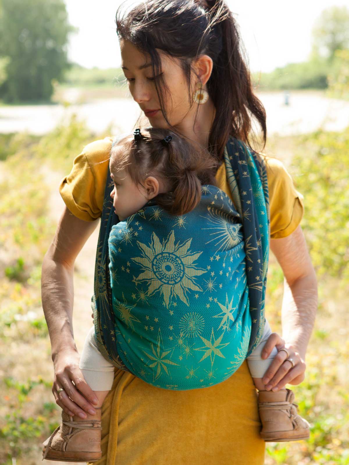 A woman carrying a child on her front in a eal woven wrap with starry pattern