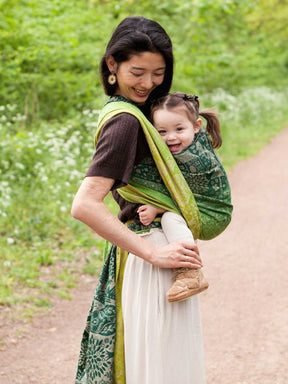 Woman carrying a baby in a green woven wrap with animal folk design.