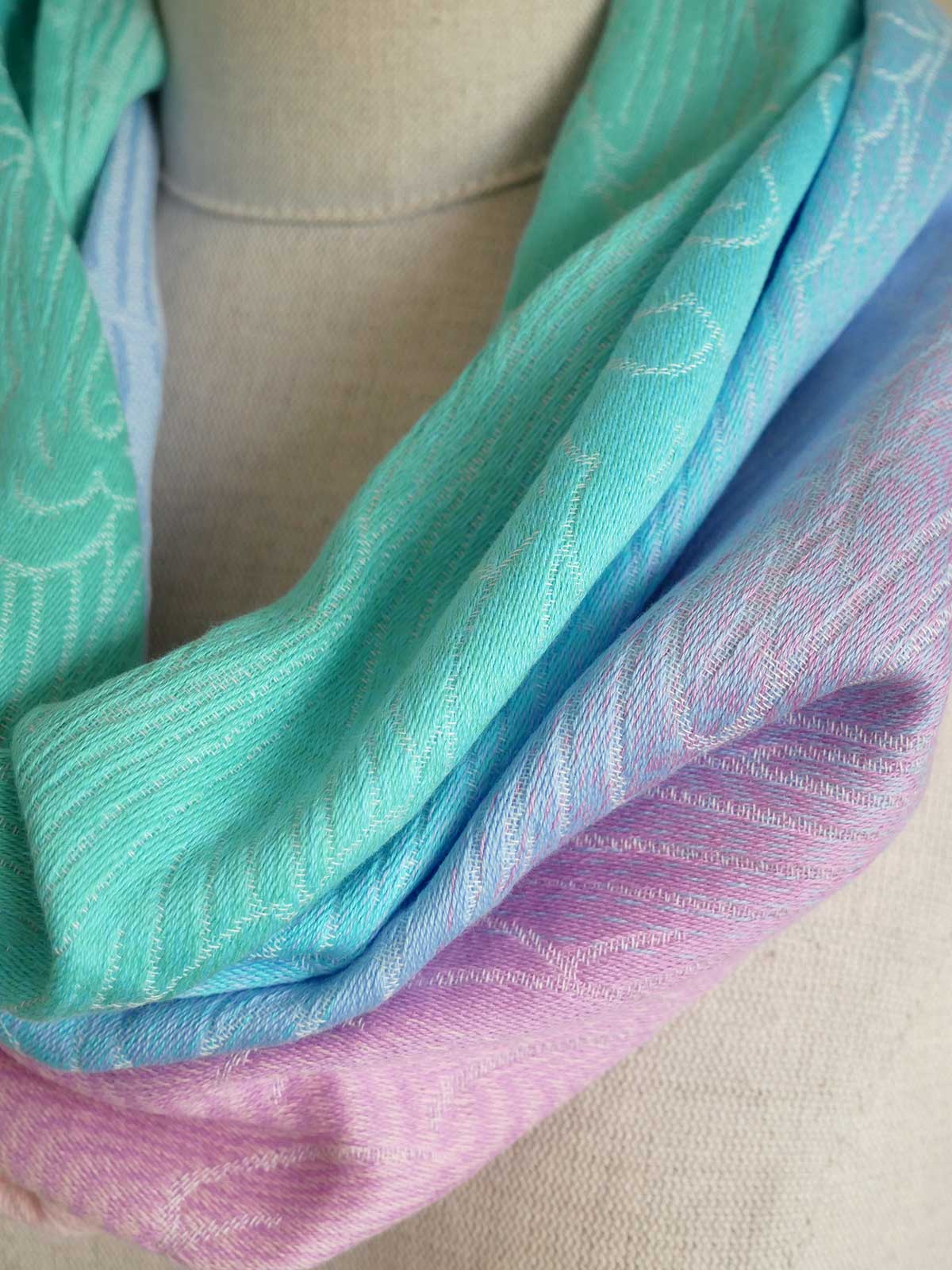 Close-up of a cowl with green, blue, and purple hues on a neutral background