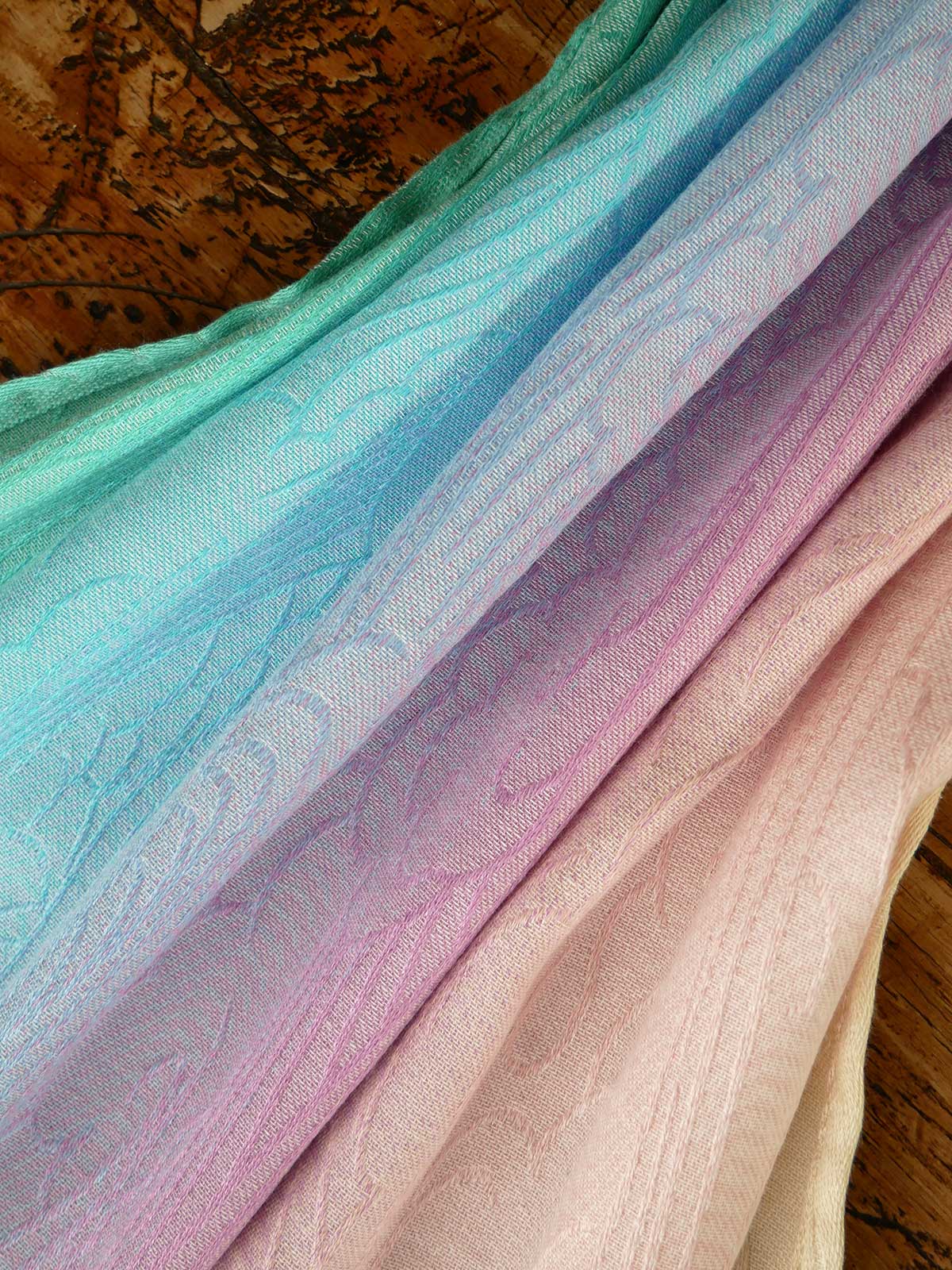 Stack of colorful fabric with a gradient from green to pink on a wooden surface.