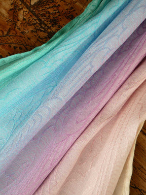 Stack of colorful fabric with a gradient from green to pink on a wooden surface.
