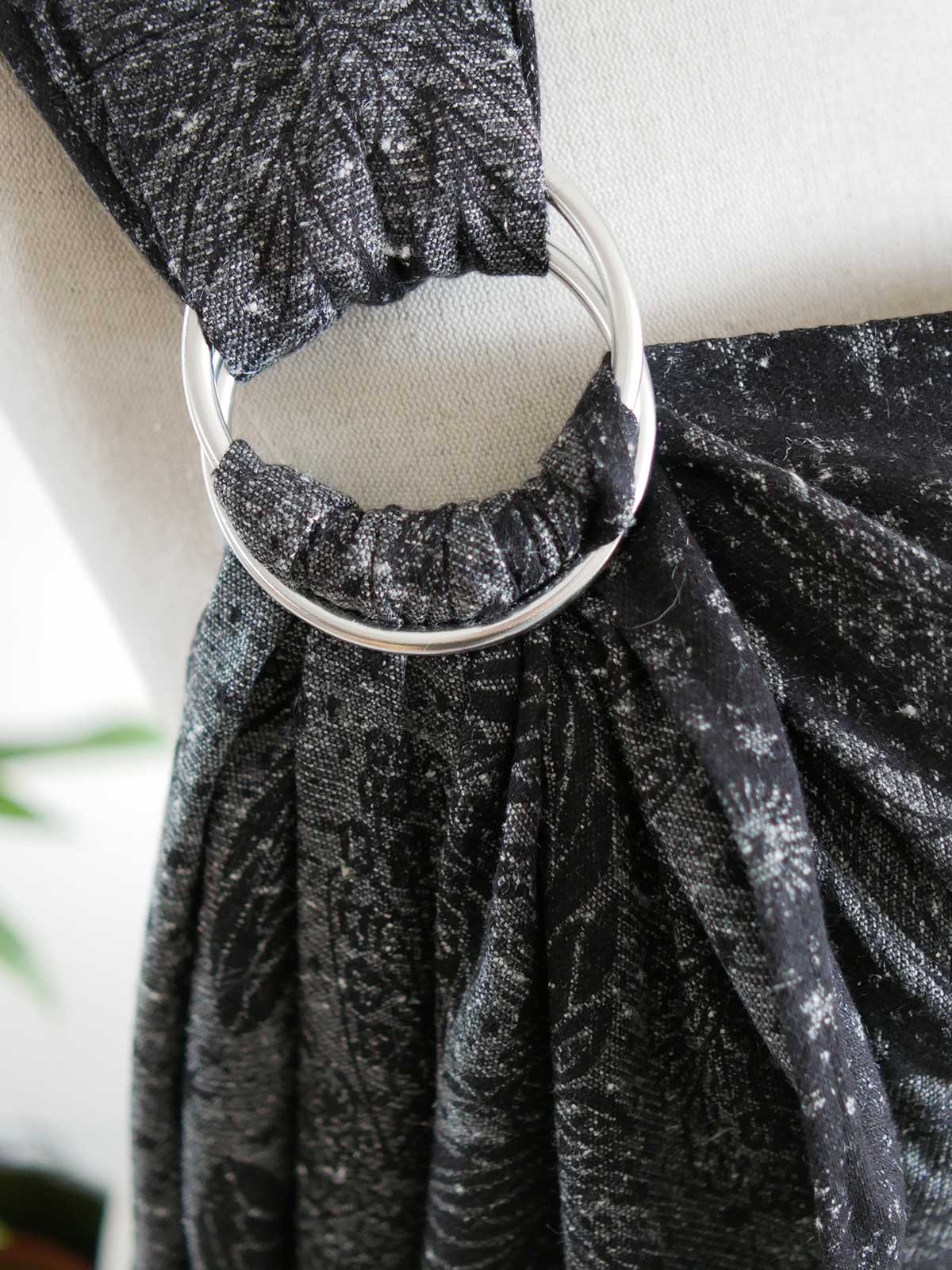 A close-up of a black and gray patterned fabric garment with a large silver metal ring detail, displayed on a cream-colored mannequin.
