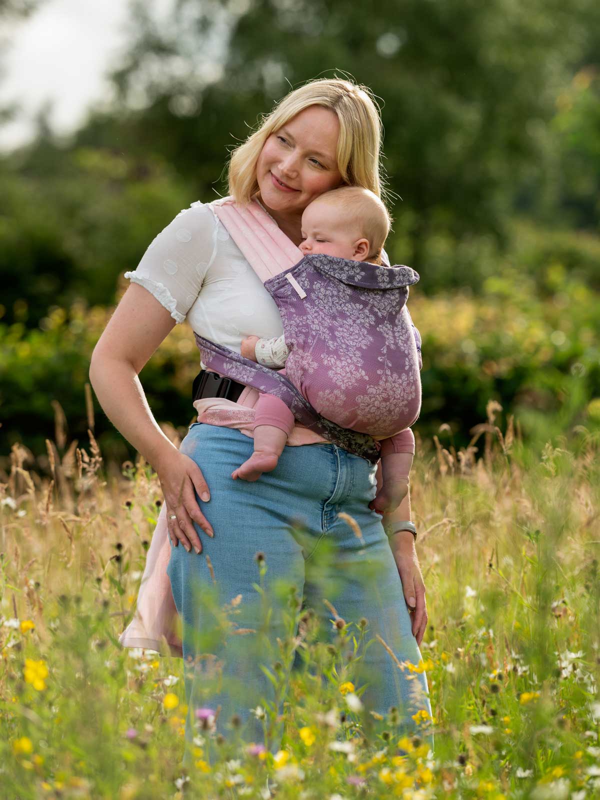 Side view of model in soft pink and purple Cairis baby carrier. 