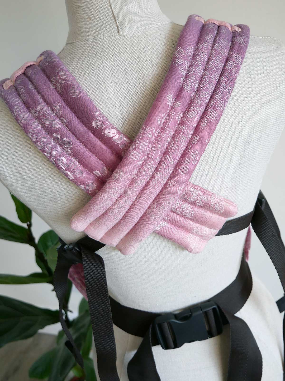Pink tbaby carrier straps on a mannequin with a blurred plant background