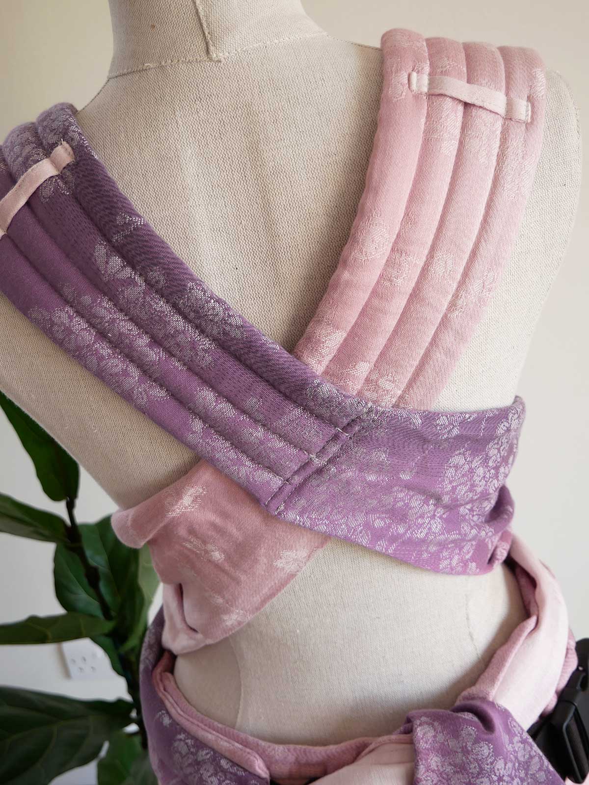 Pink and purple baby carrier on a mannequin with a plant in the background