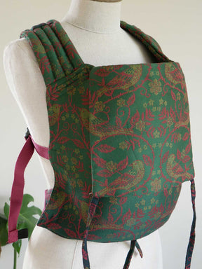 Green and red patterned baby carrier on a mannequin against a white background