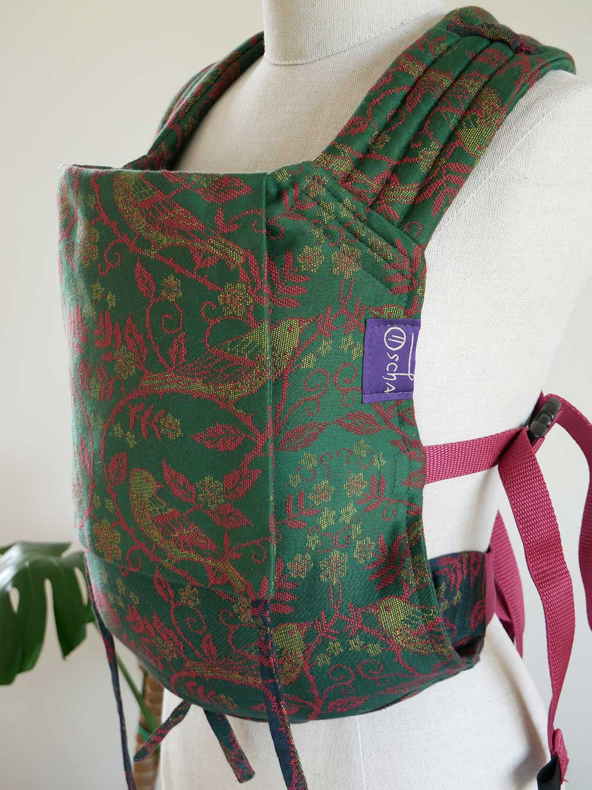 Green and red patterned baby carrier on a mannequin with a visible brand label.