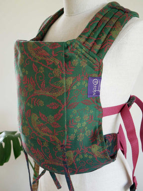 Green and red patterned baby carrier on a mannequin with a visible brand label.