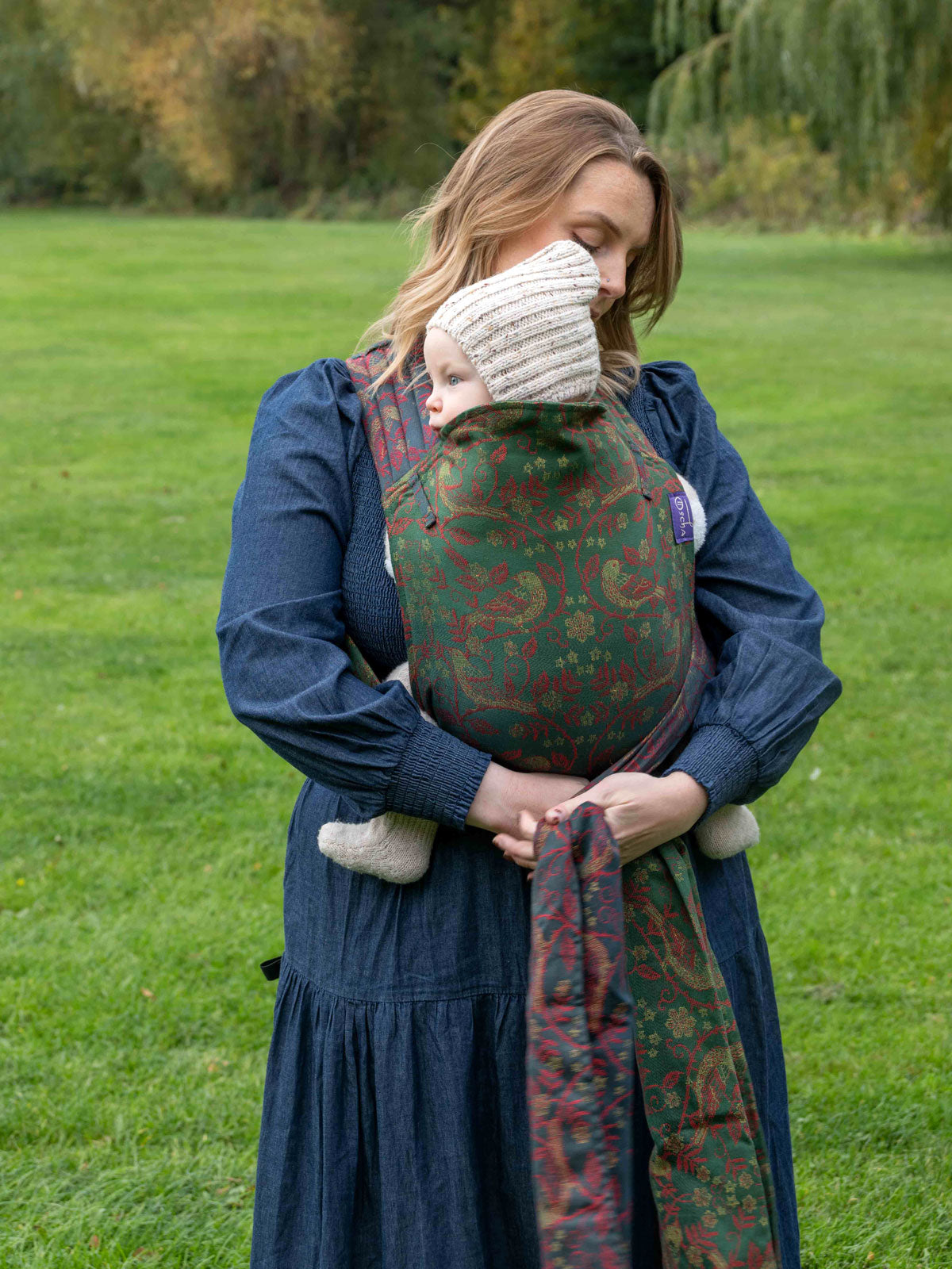Woman carrying a child in a baby carrier outdoors on a grassy field