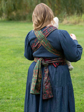 Person wearing a blue dress with a colorful baby carrier outdoors on a grassy area