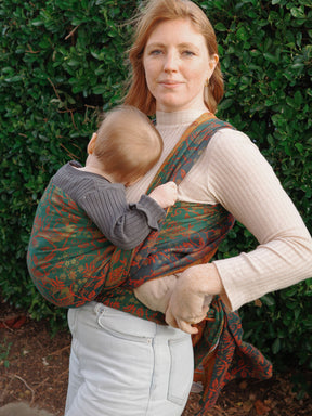 Woman carrying a baby in a sling against a green bush background