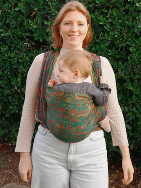 Woman carrying a baby in a floral baby wrap against a green leafy background