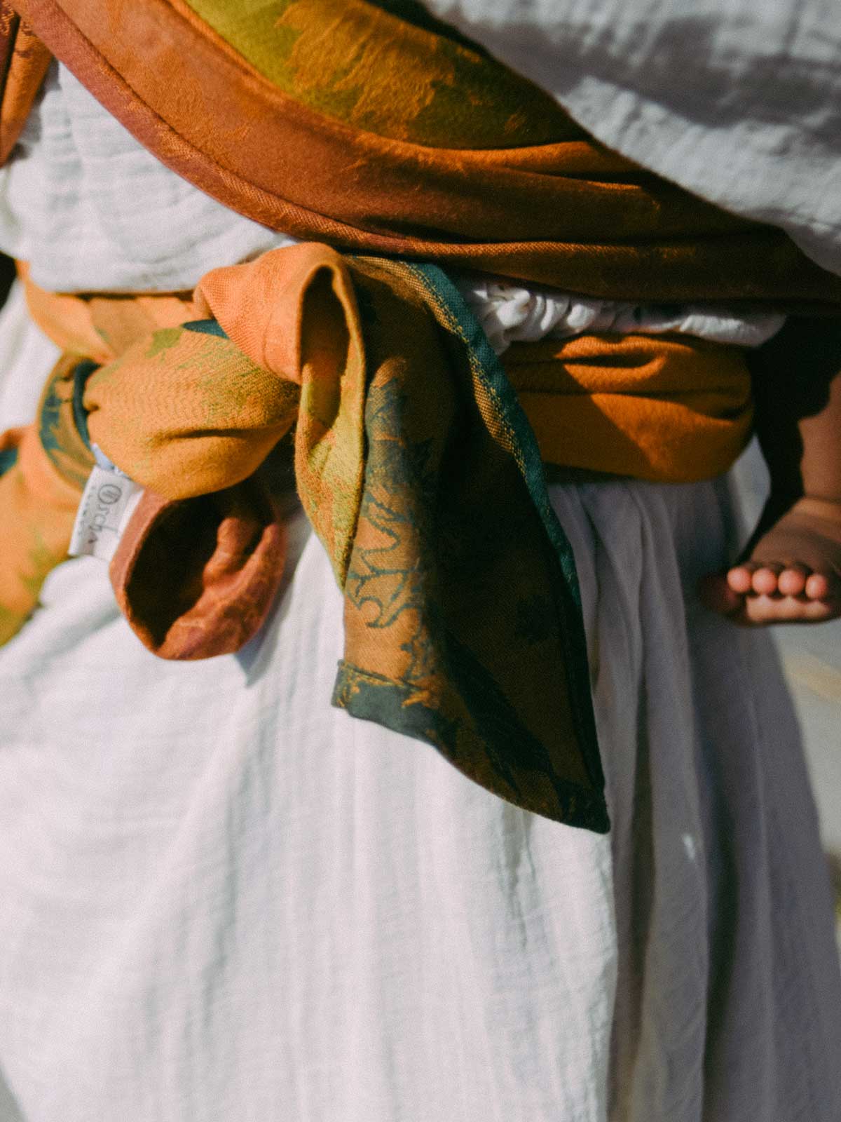 Close-up of a person wearing a brown and green patterned baby wrap. 
