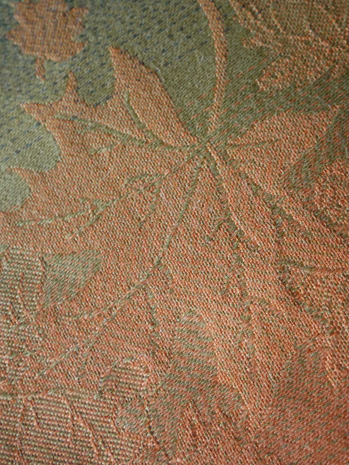 Close-up of a textured fabric with leaf pattern in green and brown tones.