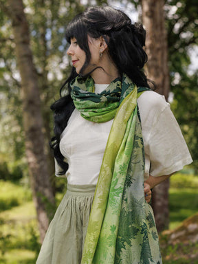 Theside view of a woman wearing a green shawl as a scarf with a leaf pattern.