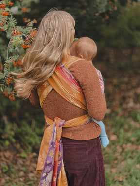 Back of a woman carrying a baby in a autumnal coloured woven wrap with leaf patterns