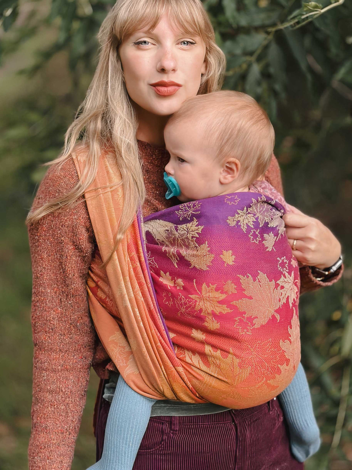 Woman carrying a baby in a autumnal coloured woven wrap with leaf patterns