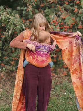 Woman wrapping a baby in a autumnal coloured woven wrap with leaf patterns