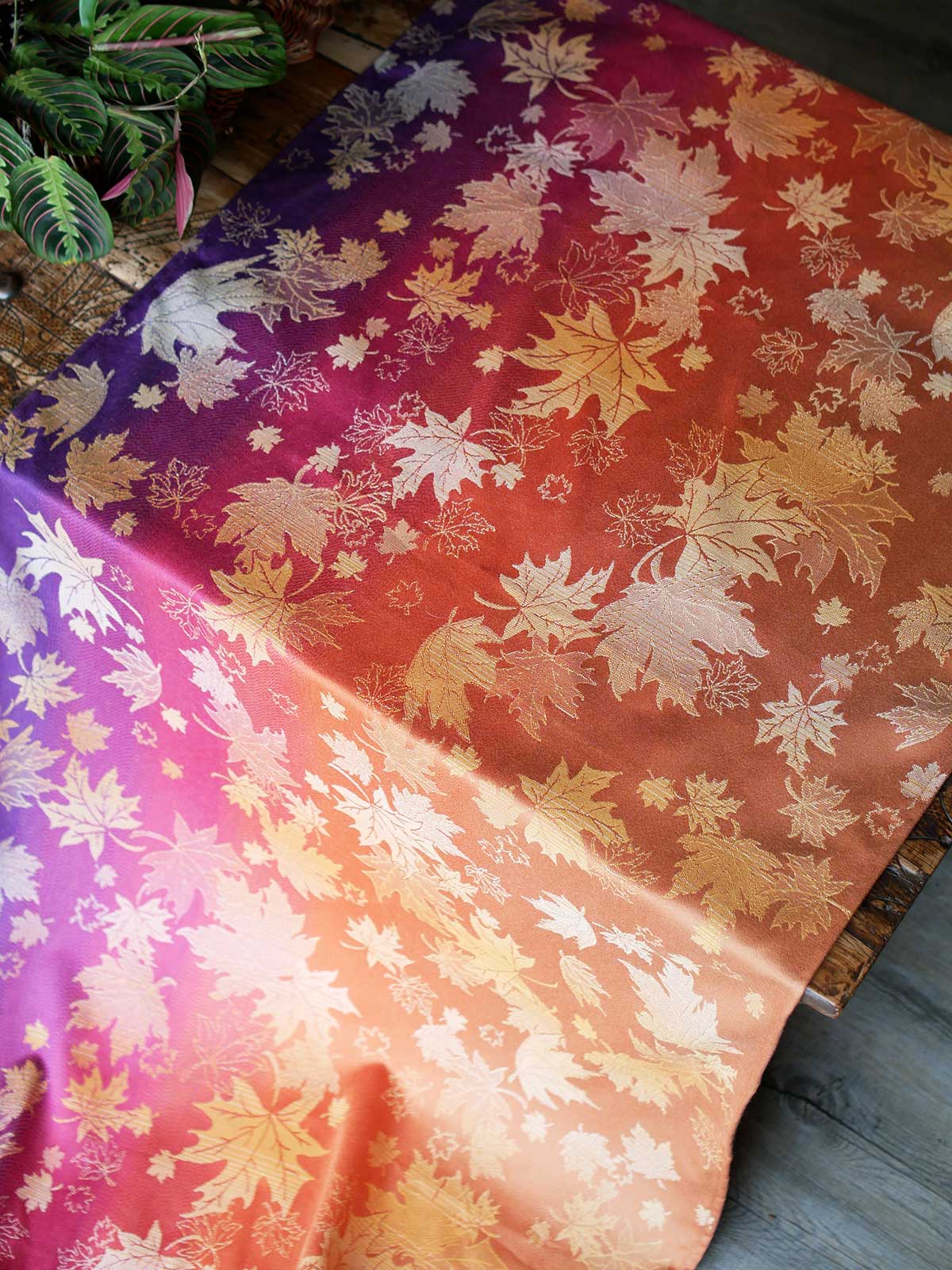Purple, pink and orange fabric with leaf patterns laid over a wooden table