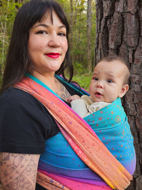 Woman holding a baby in a colorful sling against a natural background