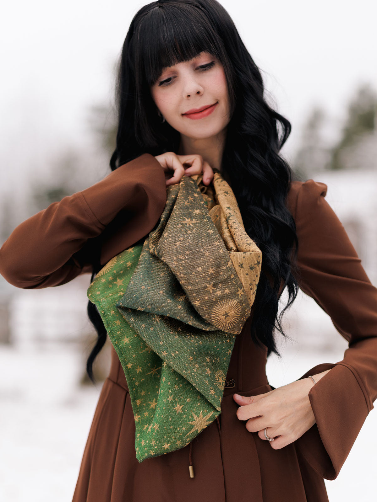 Woman holding a green and brown patterned cowl in a snowy outdoor setting