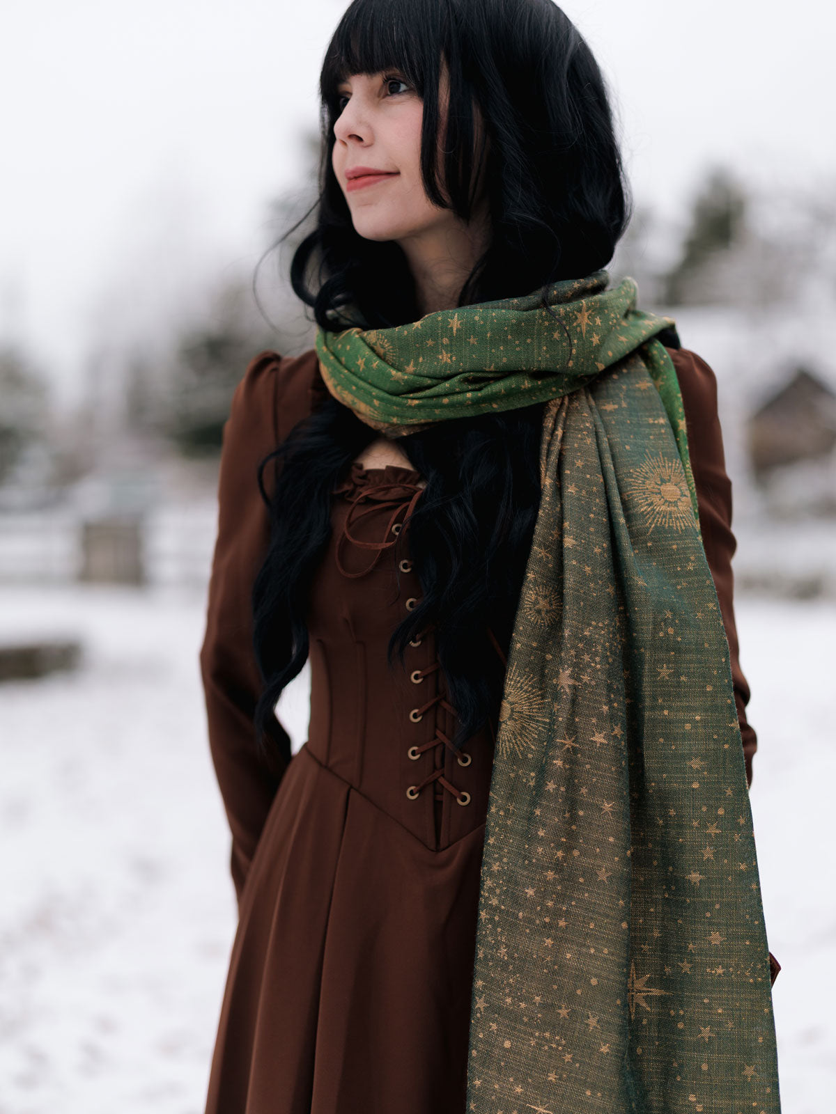 Woman wearing a brown coat and green scarf in a snowy setting