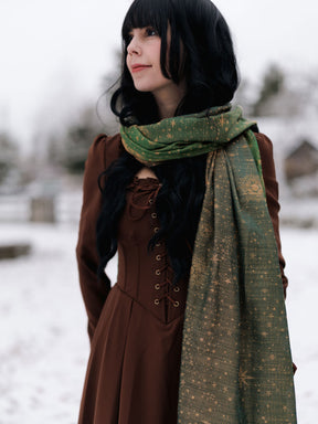 Woman wearing a brown coat and green scarf in a snowy setting
