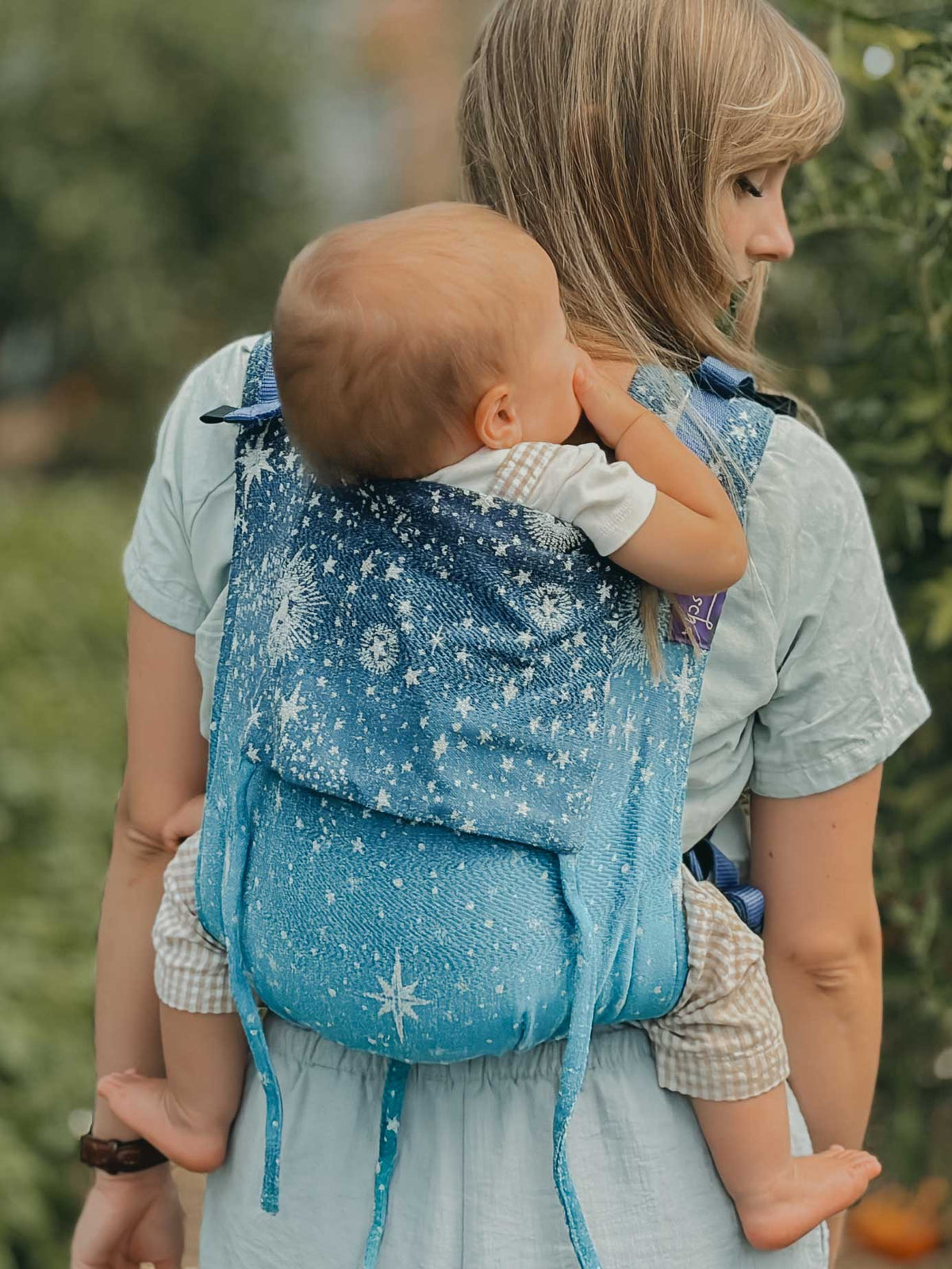 A baby being carried on the model's back in a blue starry fabric. 
