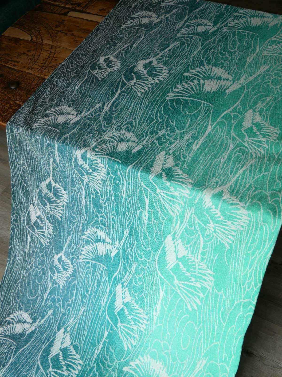 Teal fabric with white cranes pattern on a wooden surface