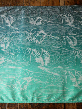 Teal fabric with white crane pattern on a wooden surface