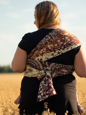 Woman carrying a child on her back with a patterned wrap in a field