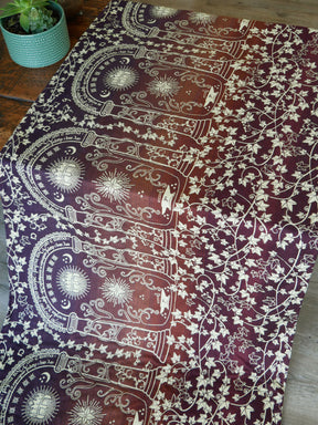 Decorative patterned fabric in dark autumnal tones on a wooden surface with a plant in the background.