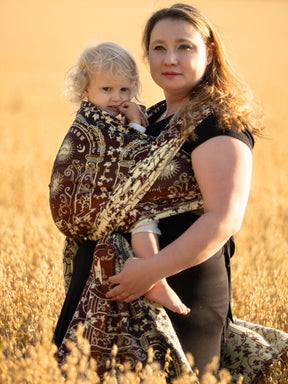 Woman holding a child in Doors of Durin Ornament Baby Wrap against a golden field background
