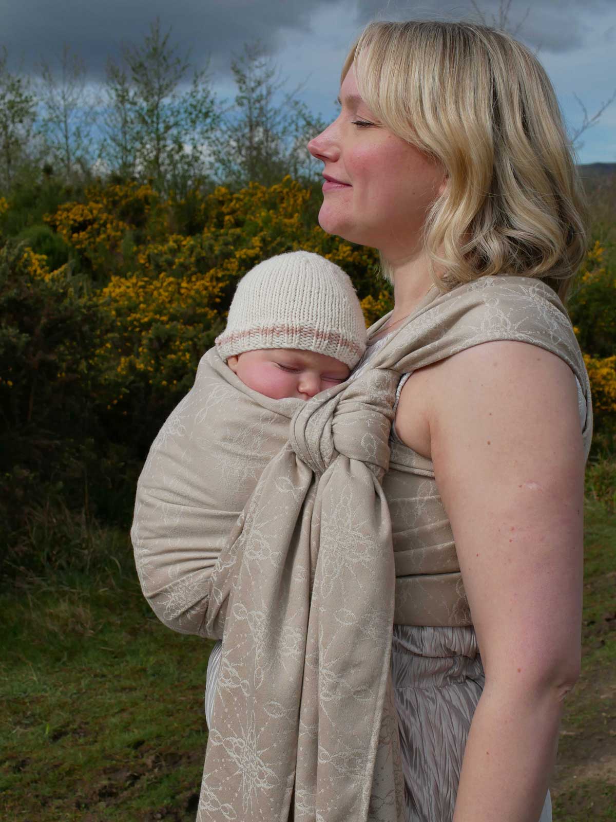 Woman with a baby in a woven wrap with a natural background
