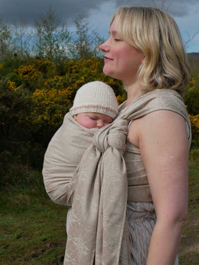 Woman with a baby in a woven wrap with a natural background