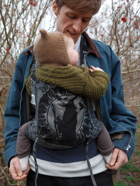 Person wearing a baby in a Gandalf the Grey Bairn Baby Carrieroutdoors with bare trees in the background