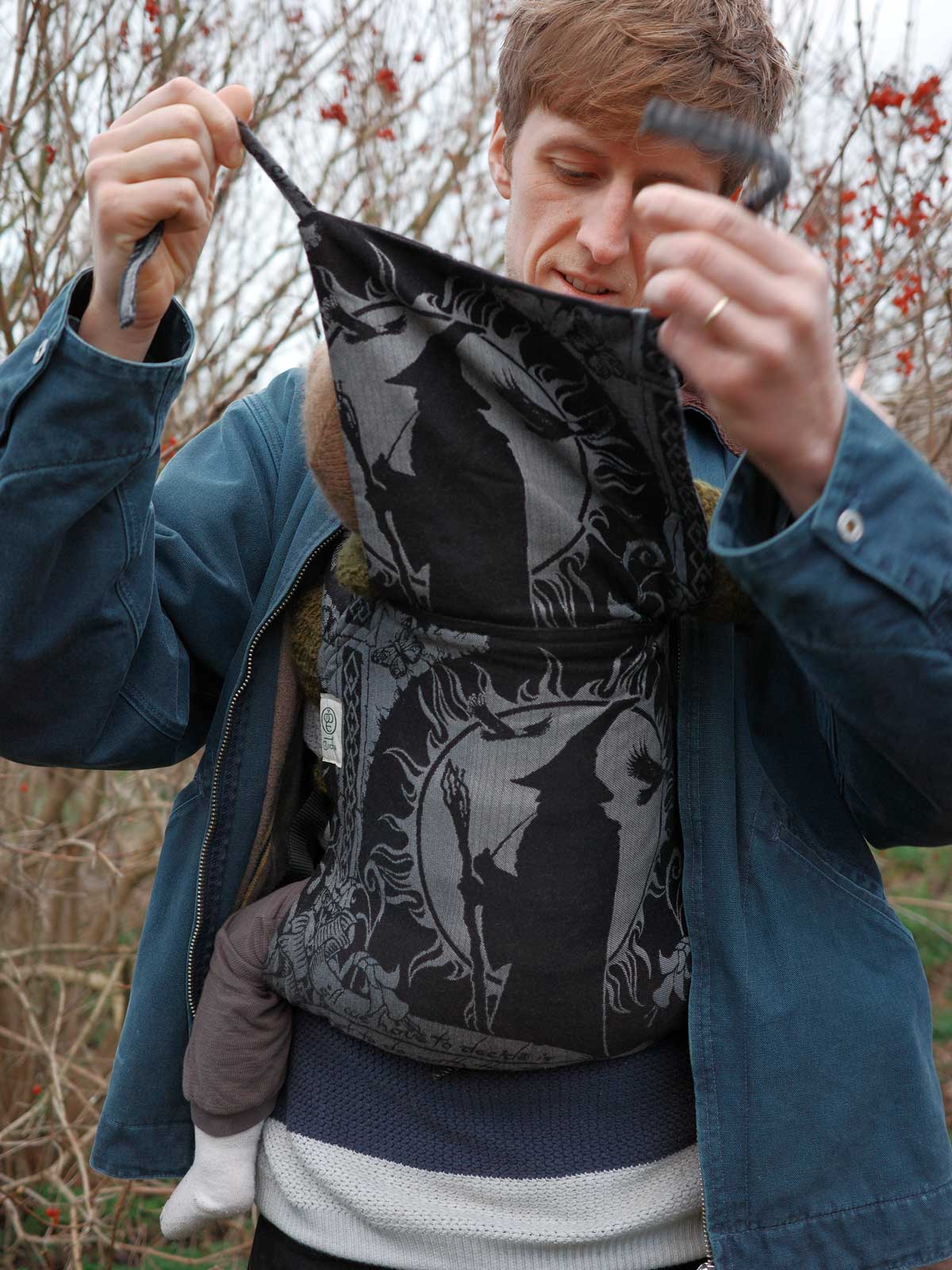 Person holding a black and gray patterned baby carrier outdoors.