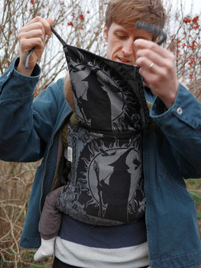 Person holding a black and gray patterned baby carrier outdoors.