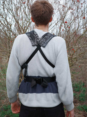 Person wearing a unique baby carrier design outdoors with bare trees in the background