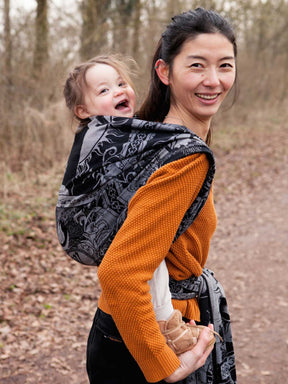 Woman carrying a child in a black patterned wrap outdoors.