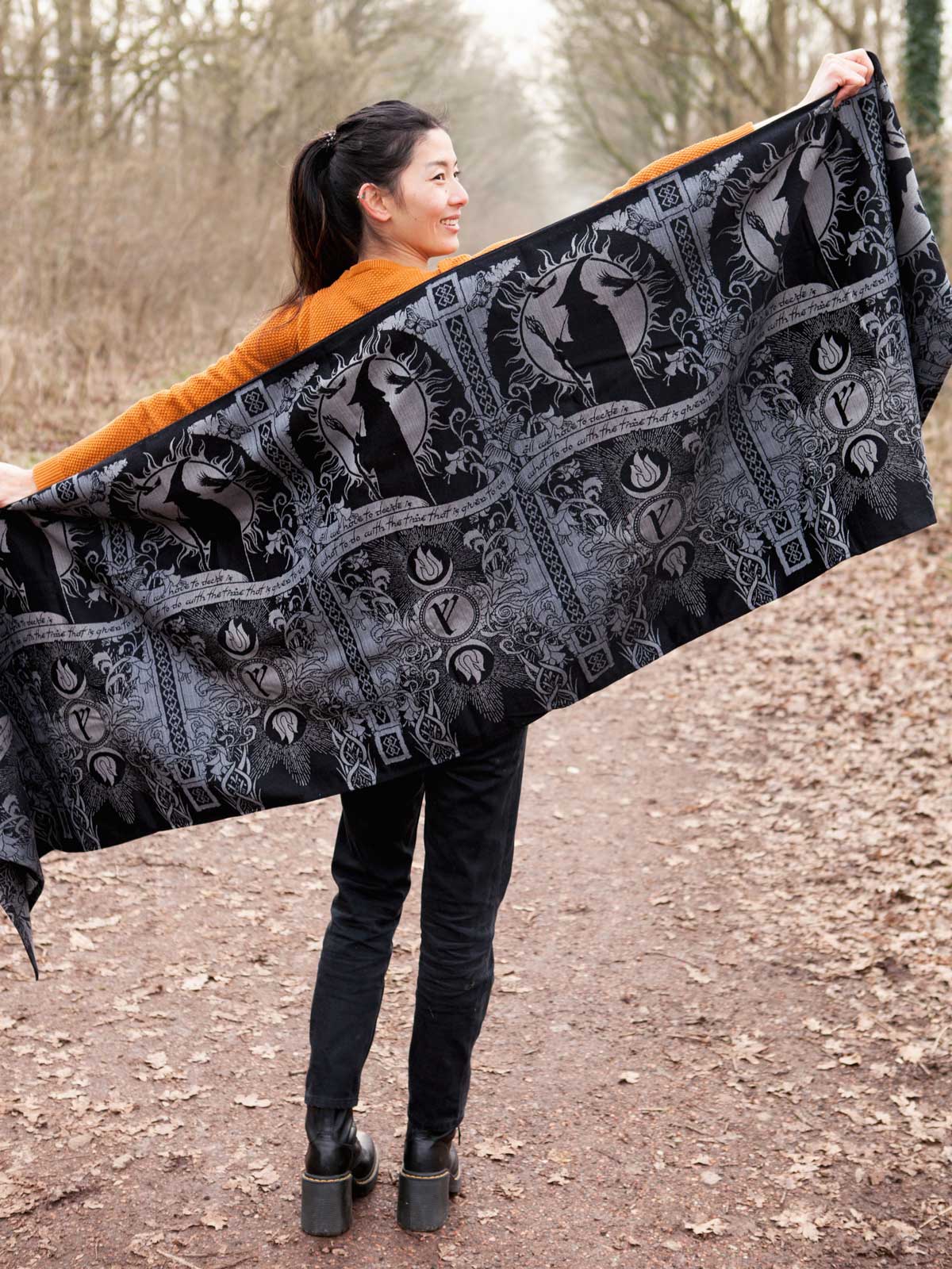 Woman holding a large black and gray patterned woven wrap outdoors.