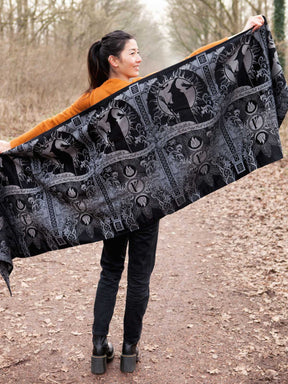 Woman holding a large black and gray patterned woven wrap outdoors.
