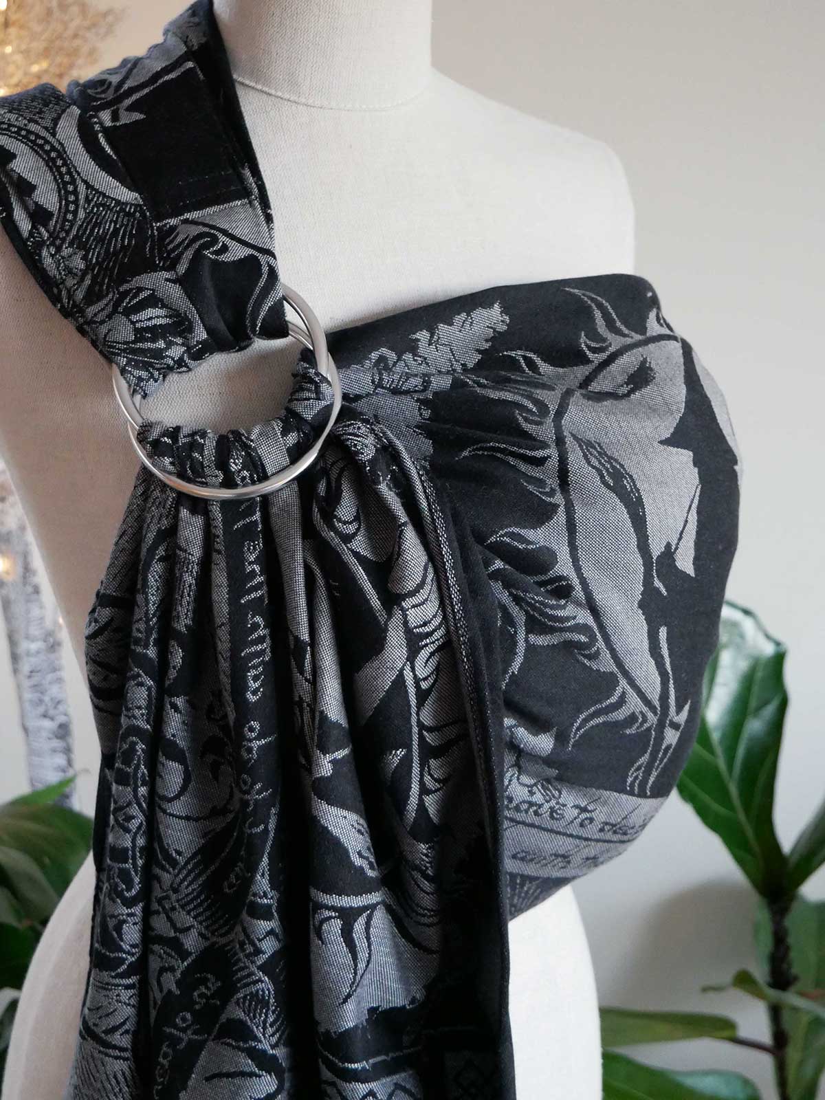 Mannequin wearing a black and gray patterned ring sling with a silver ring on a white background