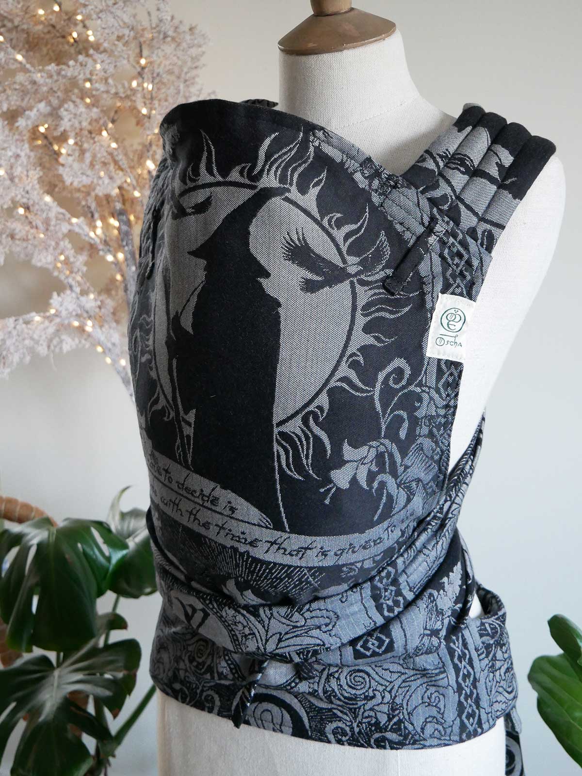 Black and gray patterned baby carrier on a mannequin with a decorative background