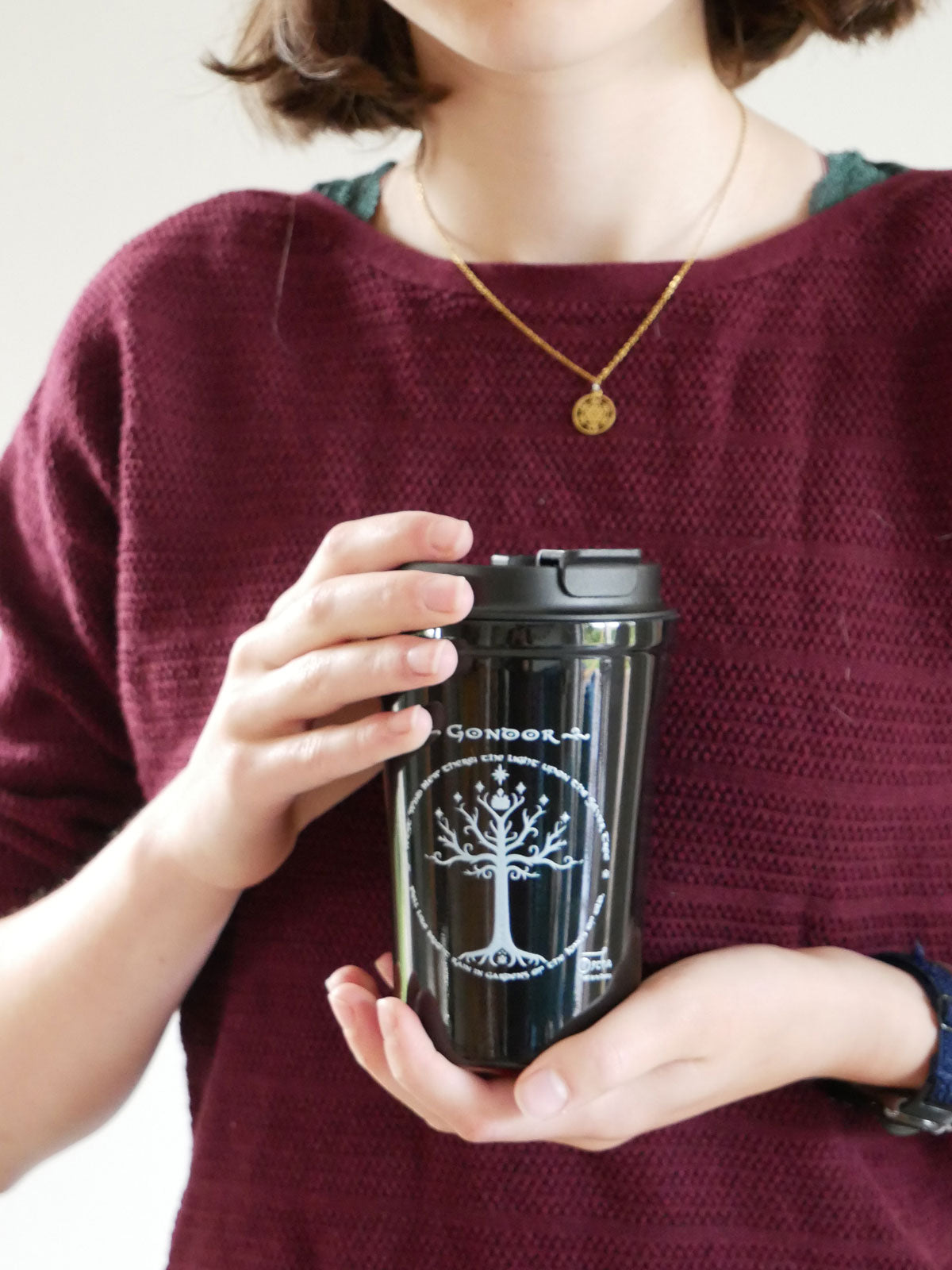 Person holding a black Gondor Travel Mug with a white design, wearing a maroon sweater.