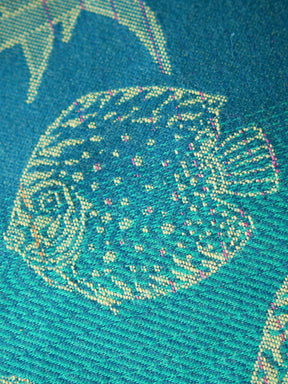 Close up of a blue teal fabric with tropical fish patten in gold