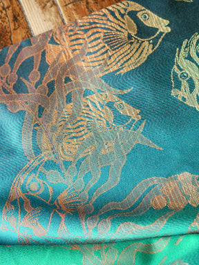 Close up of a blue teal fabric with tropical fish patten in gold and orange