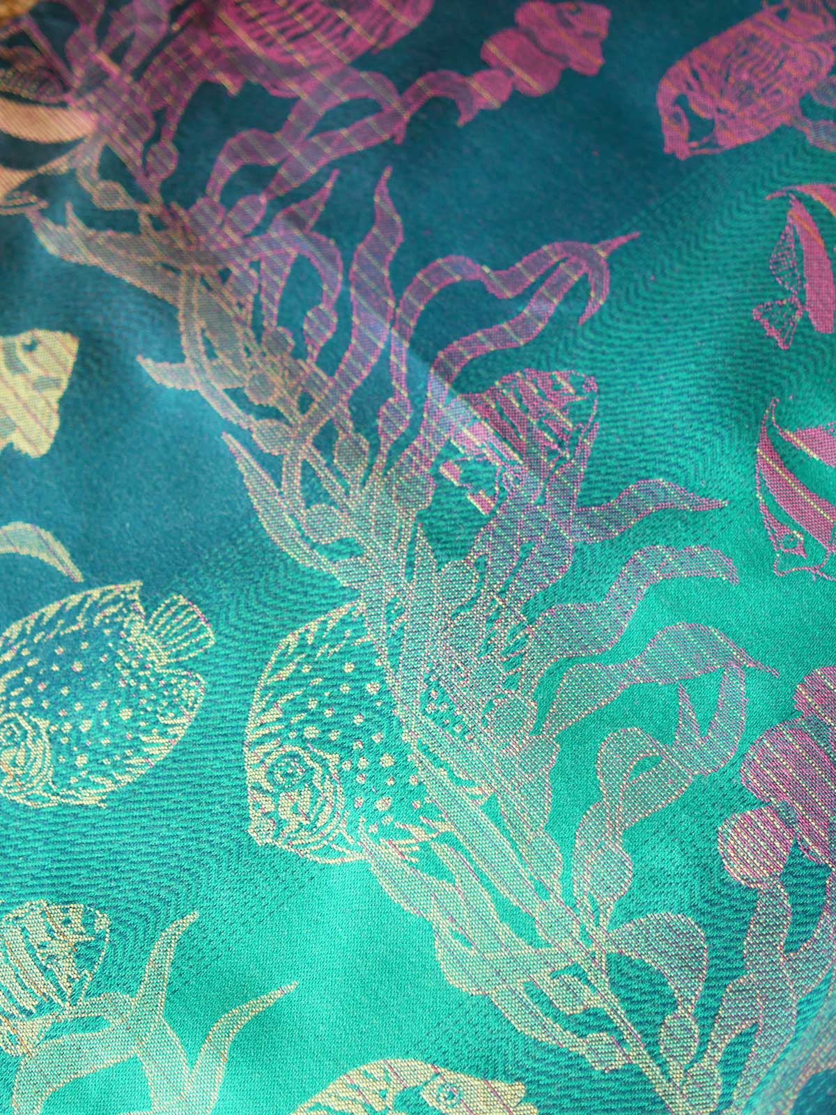 Close up of a blue teal fabric with tropical fish patten in gold and pink