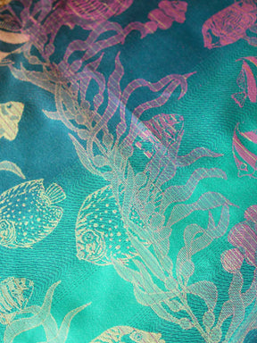 Close up of a blue teal fabric with tropical fish patten in gold and pink